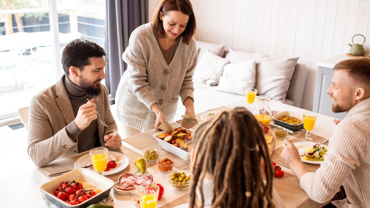 Smiling friends enjoy a delicious indoor brunch with fresh fruit and conversation around a table.